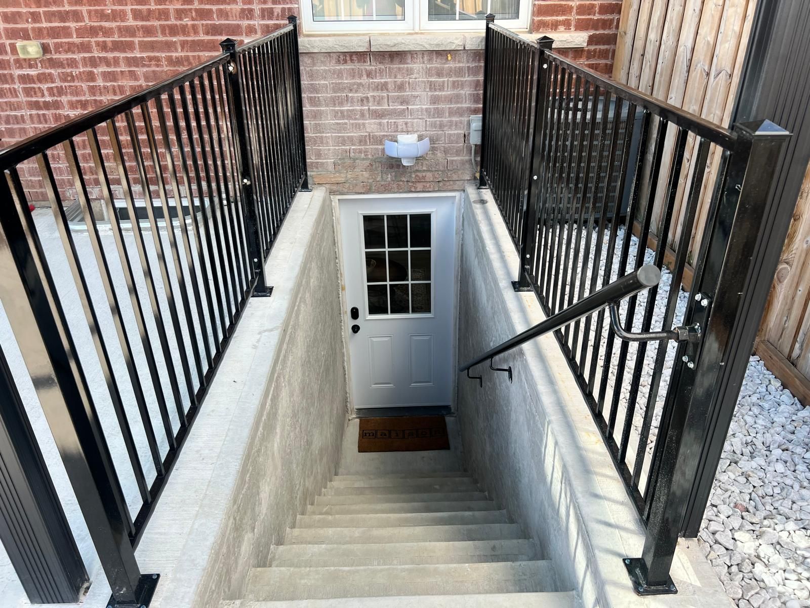 Un escalier avec des rampes en métal noir, une porte blanche et une petite fenêtre en haut.