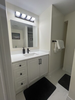 Een badkamer met een witte wastafel, een spiegel en een zwarte badmat.