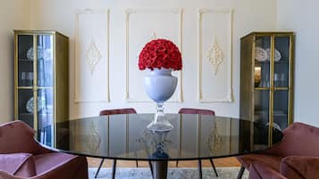 Un comedor con una mesa redonda de vidrio, rosas rojas en un florero blanco y dos aparadores con puertas de cristal.