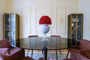 A dining area with a round glass table, red roses in a white vase, and two sideboard cabinets with glass doors.