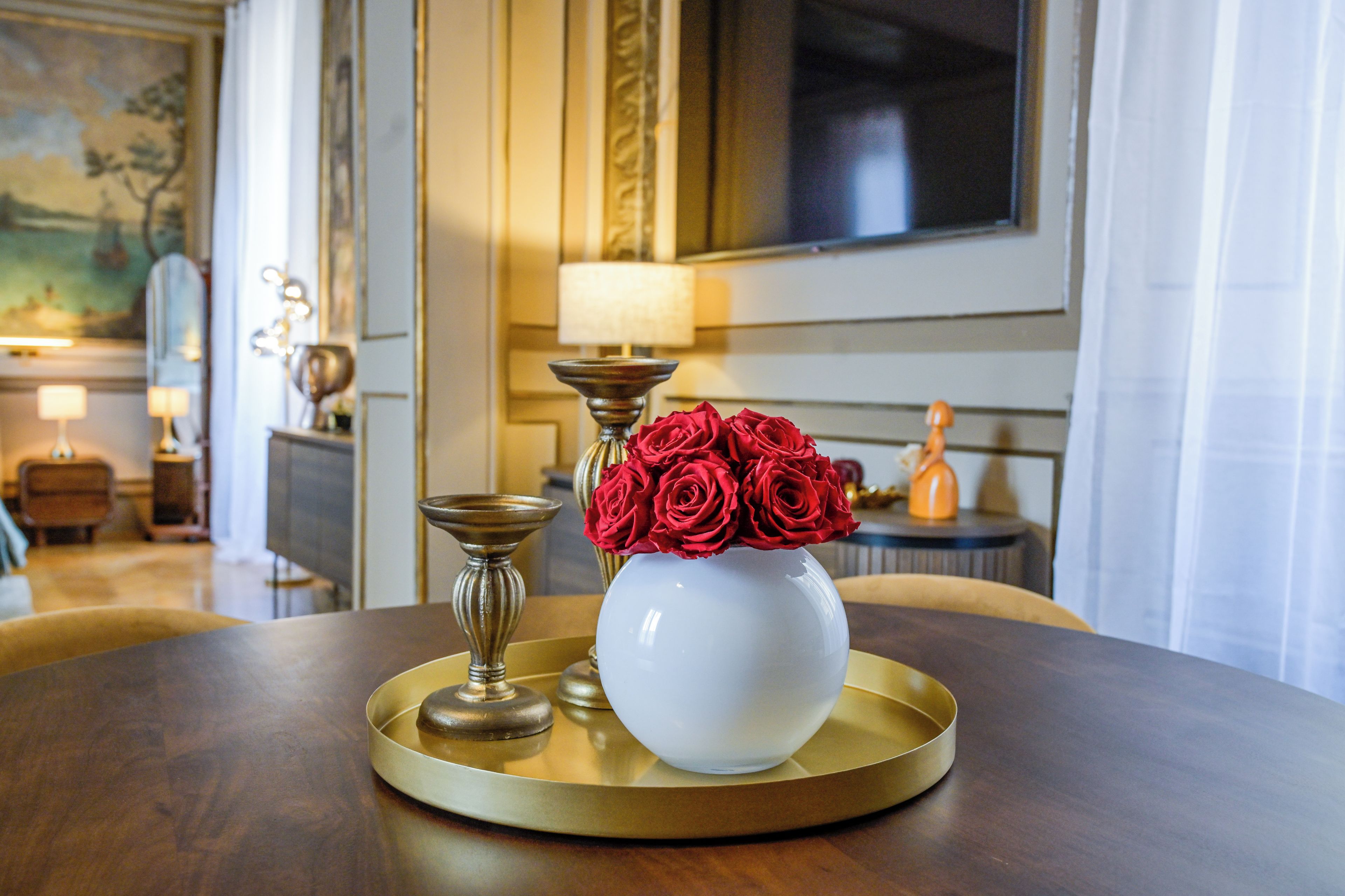 A table with a white vase containing red roses, a candle, and a tray.