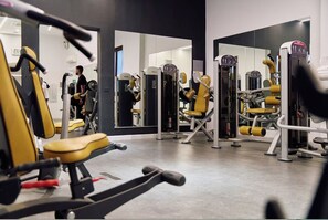 Une salle de sport équipée de matériel d’exercice, de miroirs, et où l’on aperçoit une personne au fond.