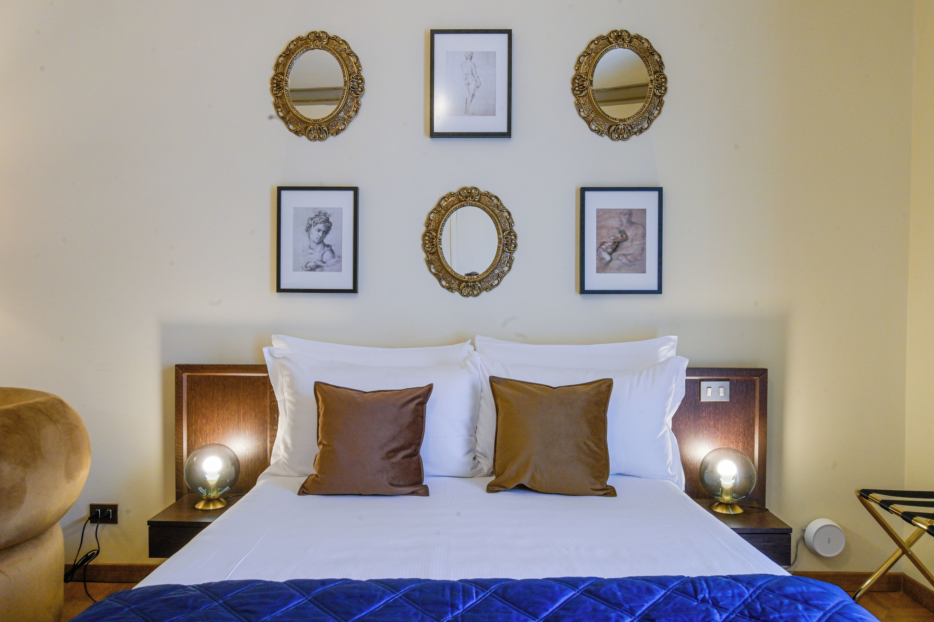 A hotel room with a bed, two nightstands, a chair, and wall-mounted mirrors and artwork.