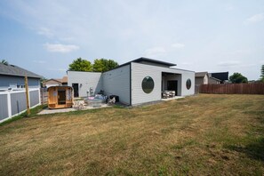 A modern single-story house with a covered patio, a hot tub, and a wooden playhouse.