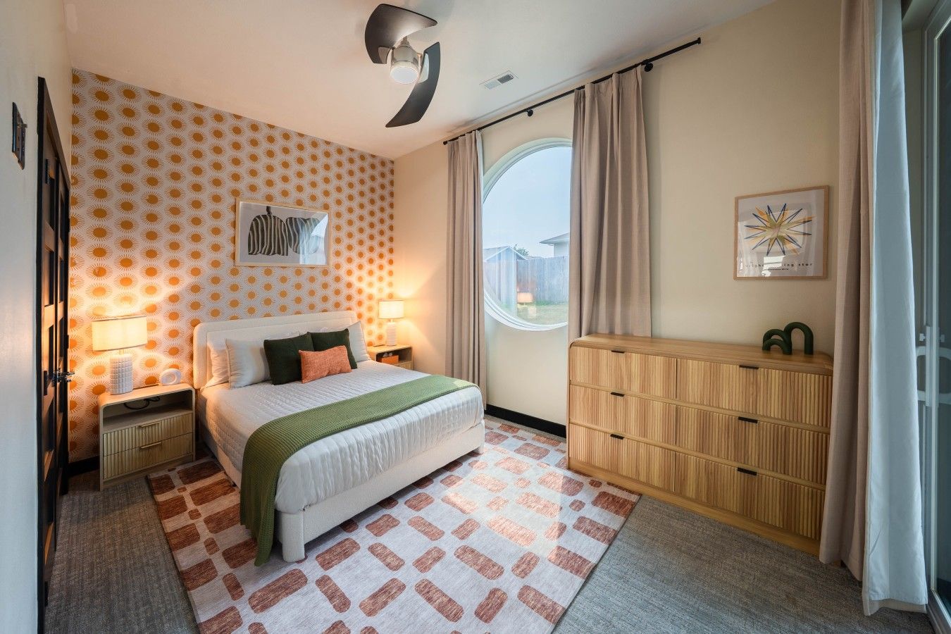 A bedroom with a bed, bedside tables, a dresser, a window with curtains, and a wall with a patterned wallpaper.