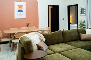 A living room with a green sofa, a dining table with chairs, and a framed picture on the wall.