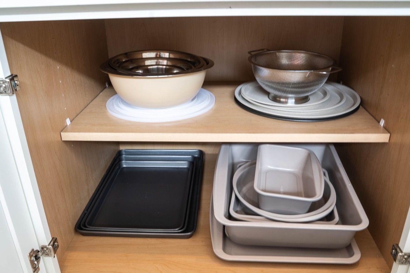 A kitchen cabinet with a black baking tray, a white bowl, and a metal strainer.