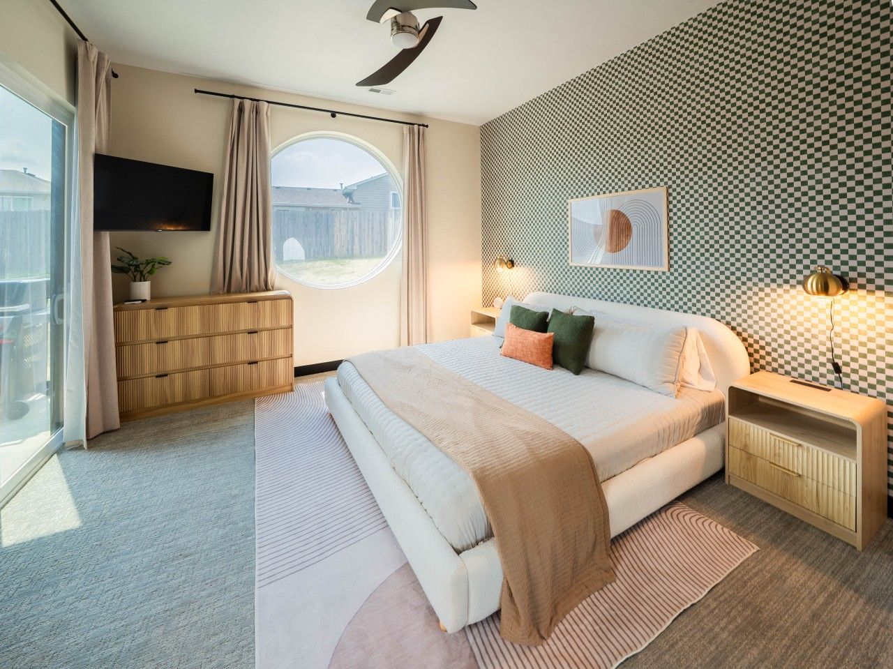 A bedroom with a bed, bedside tables, a TV, a window, and a view of the outside.