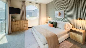 A bedroom with a bed, bedside tables, a TV, a window, and a view of the outside.