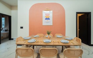 A dining area with a table set for six, surrounded by wicker chairs, with a framed artwork above the table. - The Metta: Cowboy Pool + Sauna, Sleeps 9 (Sioux Falls)