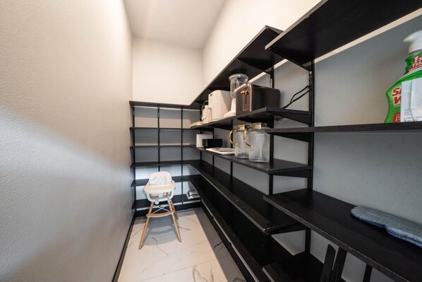 A narrow hallway with black shelving units, a white chair, and a bottle of hand sanitizer on the right.