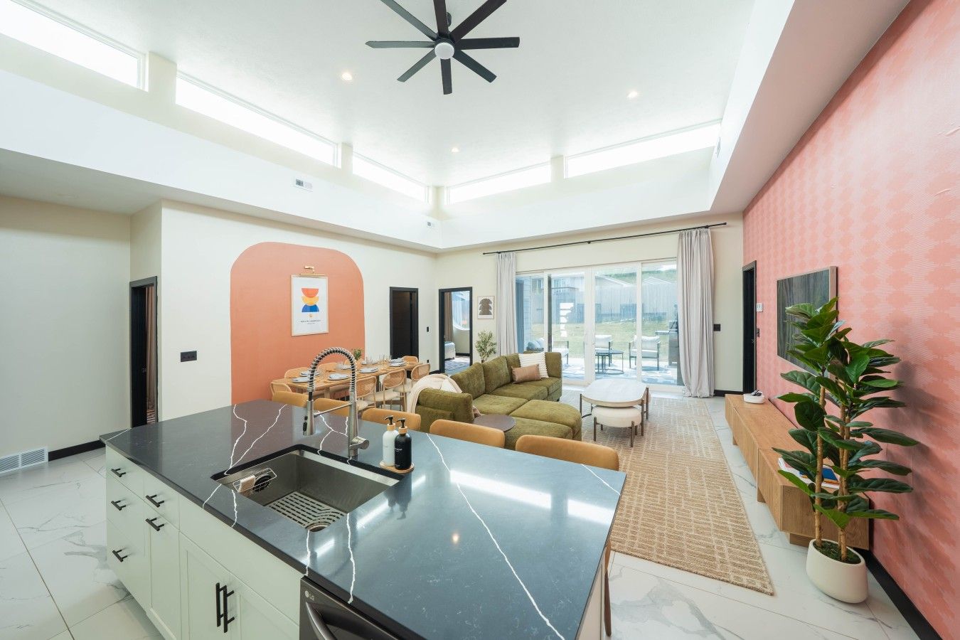 Eine moderne Küche mit schwarzem Arbeitsplatz, weißen Schränken und einer eingebauten Spüle. Es gibt einen Essbereich mit Tisch und Stühlen, und ein großes Fenster mit Blick ins Freie.