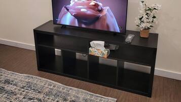 Ein Flachbildfernseher auf einer schwarzen Unterhaltungsecke, neben dem ein Blumenarrangement steht.