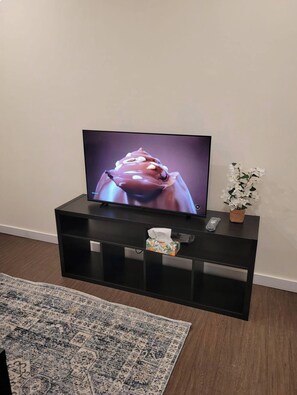 A flat-screen TV on a black entertainment unit with a floral arrangement beside it. - Beacon Suite (Edmonton)