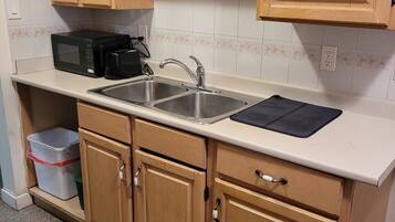 A kitchen with wooden cabinets, a double sink, a microwave, and a coffee maker.