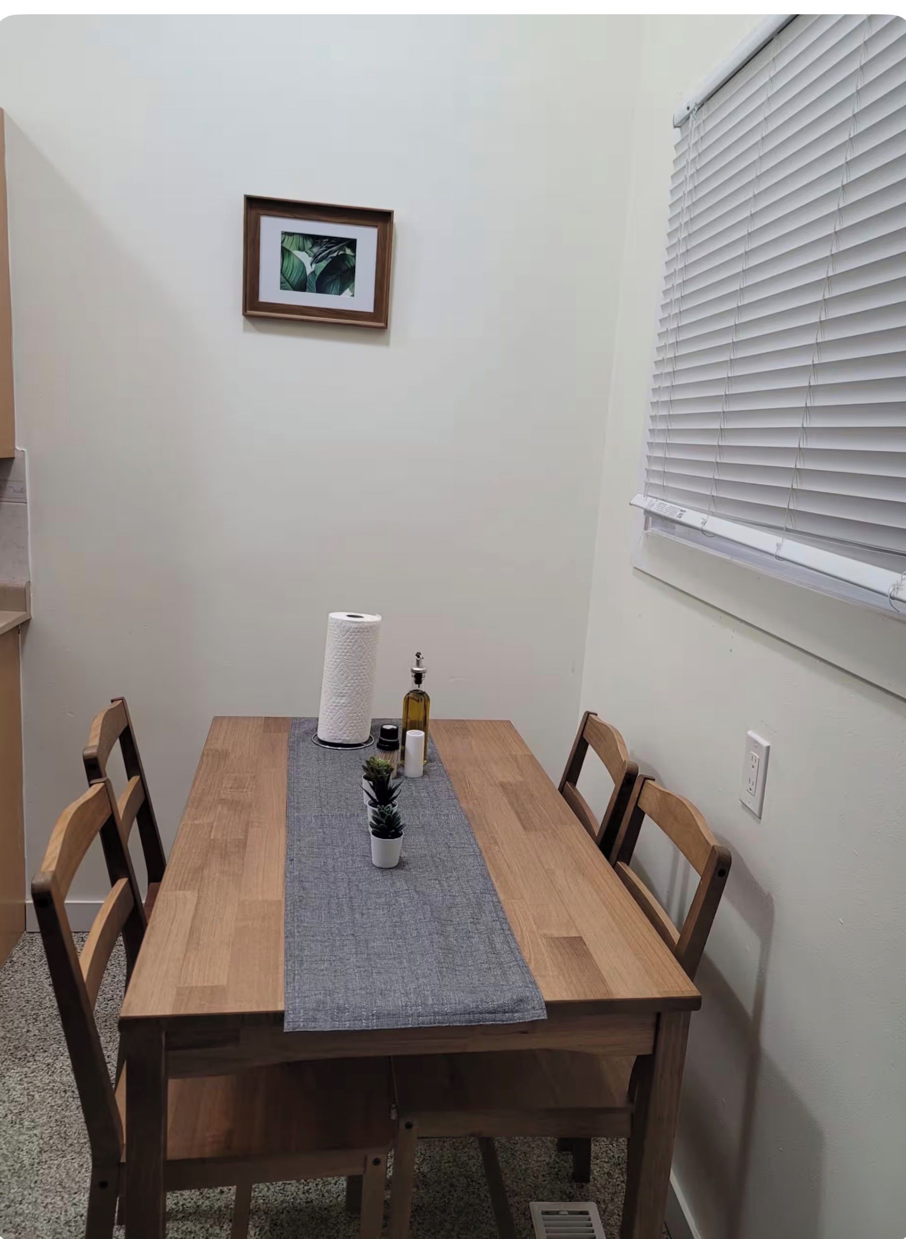 A dining table with a grey placemat, surrounded by wooden chairs. A framed picture hangs on the wall above the table.