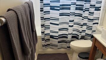 Un baño con inodoro, cortina de ducha, toallero, cubo de basura y un estante pequeño con artículos de aseo.