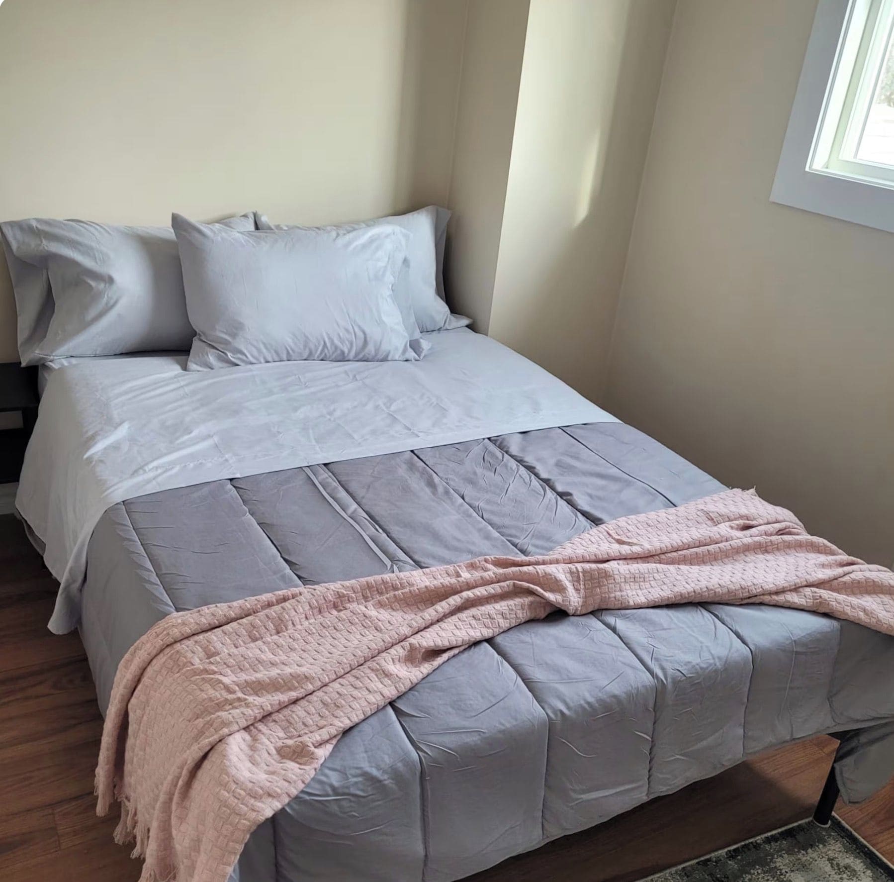Ein Bett mit einer grauen Bettdecke, Kissen und einer rosa Decke.
