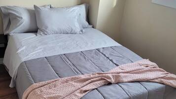 A bed with a grey duvet, pillows, and a pink blanket.