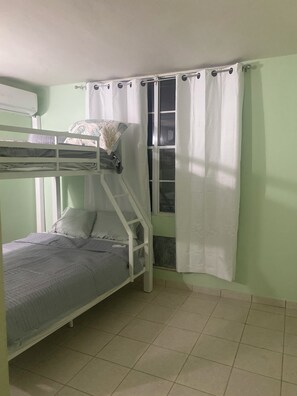 Una cama litera con ventana y cortinas, un radiador y suelo de baldosas.