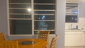 A dining area with a wooden table and chairs, a window with a view of the outside, and a kitchen area with a sink and cabinets. - Charming 3-bedroom apartment minutes from beach in fajardo ! (Fajardo)