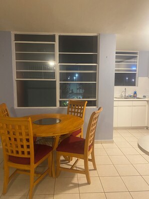 Un comedor con mesa y sillas de madera, una ventana con vistas al exterior y una zona de cocina con lavabo y armarios.