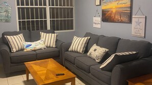 A living room with two grey sofas, a wooden coffee table, and a window with bars. - Charming 3-bedroom apartment minutes from beach in fajardo ! (Fajardo)