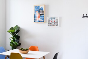 A room with a white table, orange and blue chairs, a potted plant, and two framed artworks on the wall. - The Jefferson: Upscale Studio Loft in Downtown SF (Sioux Falls)