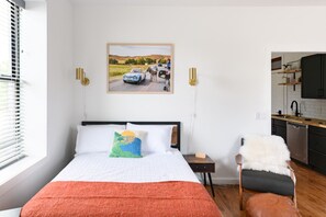 A bedroom with a bed, a nightstand, a chair, and a painting on the wall. - The Jefferson: Upscale Studio Loft in Downtown SF (Sioux Falls)
