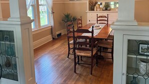 Zona pranzo con tavolo e sedie in legno, lampadario e finestra con tende.
