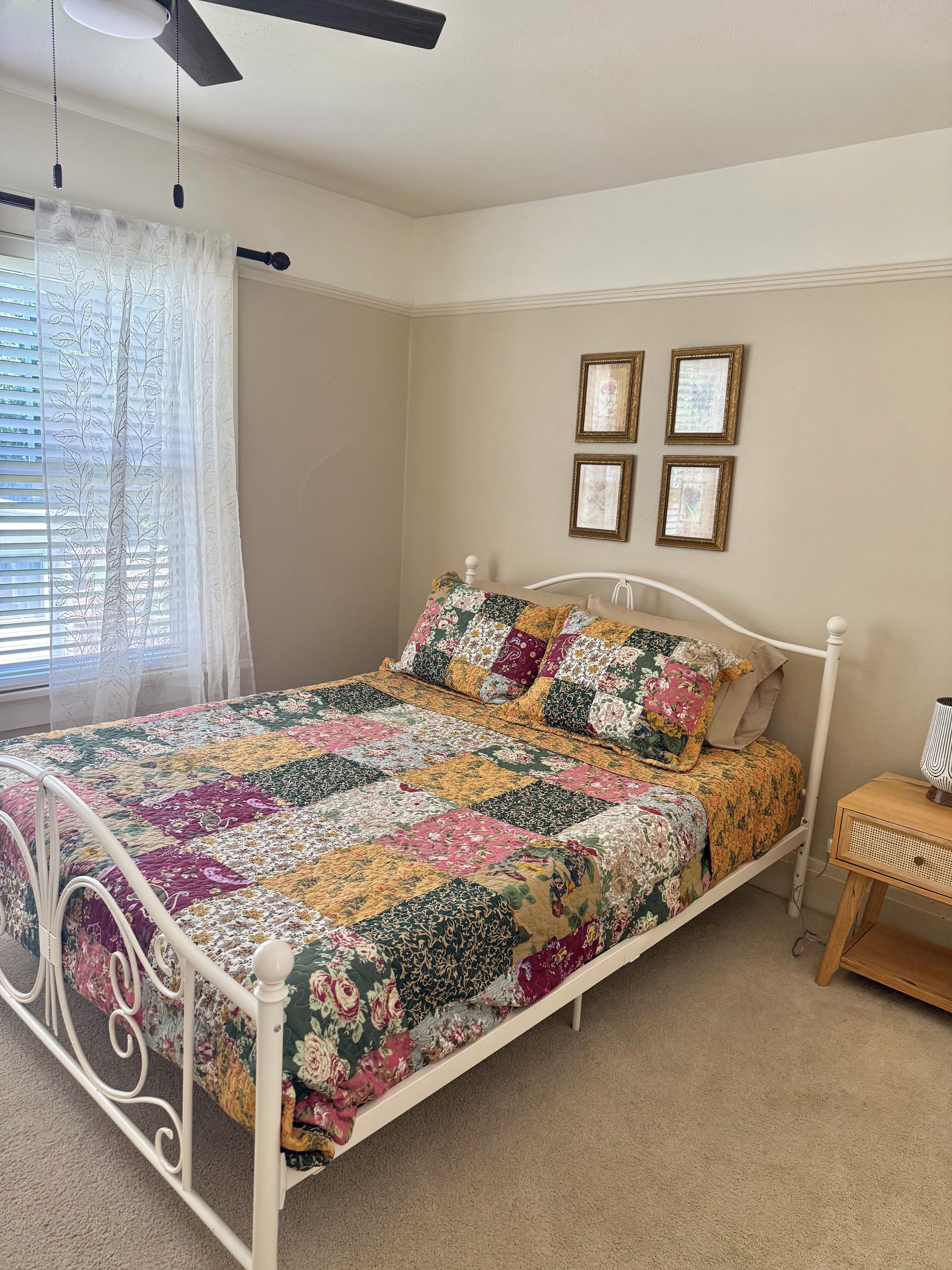 A bed with a floral quilt, a ceiling fan, and a bedside table with a lamp.