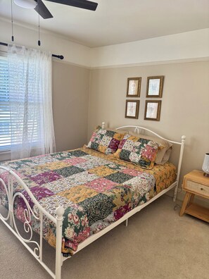 A bed with a floral quilt, a ceiling fan, and a bedside table with a lamp.