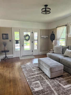 A living room with a grey sofa, a patterned rug, a wooden floor, and a door with a wreath.