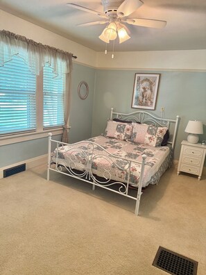 A bedroom with a bed, a nightstand, a lamp, a ceiling fan, and a window with blinds. - Santuary on Fourth (Waverly)