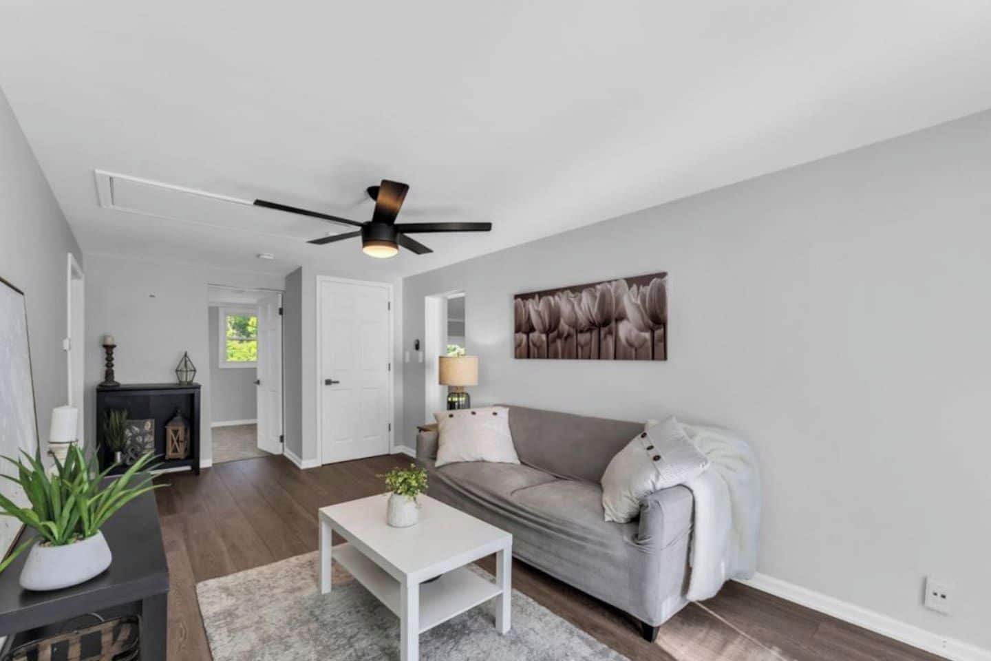 A spacious living room with a grey sofa, a white coffee table, and a ceiling fan.