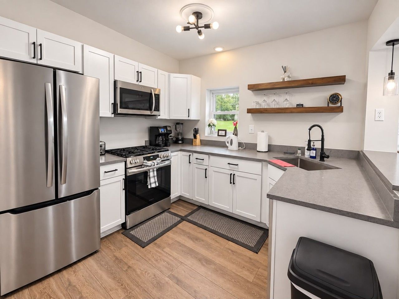 A modern kitchen with stainless steel appliances, white cabinetry, and a wooden floor.