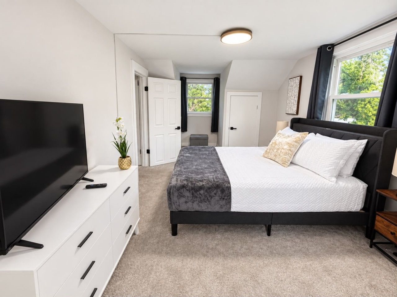 Un dormitorio con cama, televisor, cómoda y ventana.