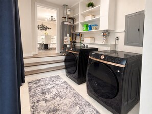Una sala de bugaderia amb dues rentadores negres, una catifa gris i una prestatgeria amb productes de neteja.