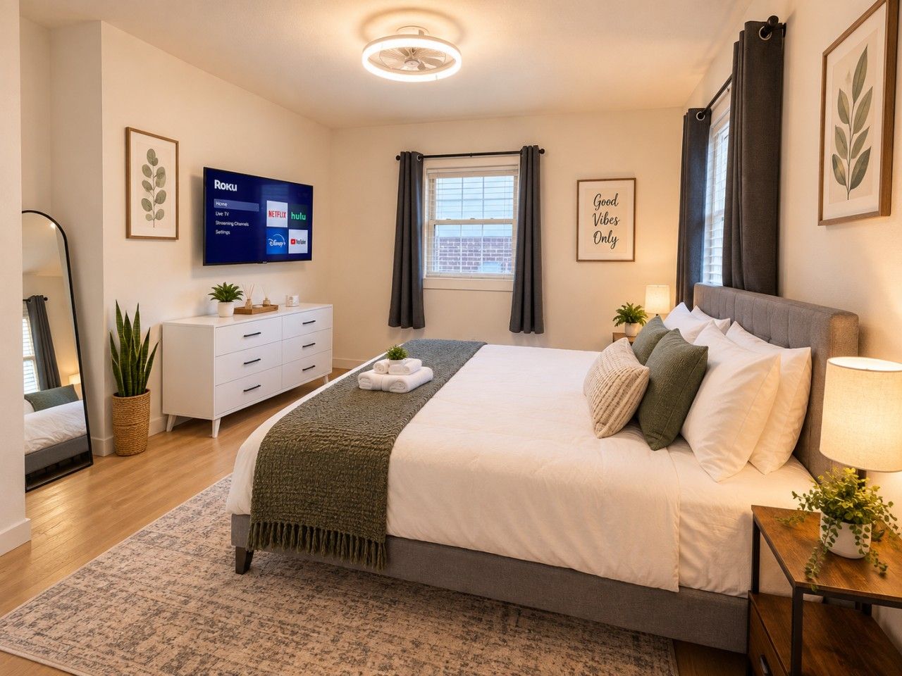 A modern bedroom with a bed, bedside table, lamp, and a TV displaying Roku channels.