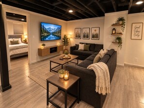A modern living room with a sofa, coffee table, and a TV displaying a mountain landscape. - Spacious Rockford Home | 4BR • 7 Beds • 4.5BA (Rockford)