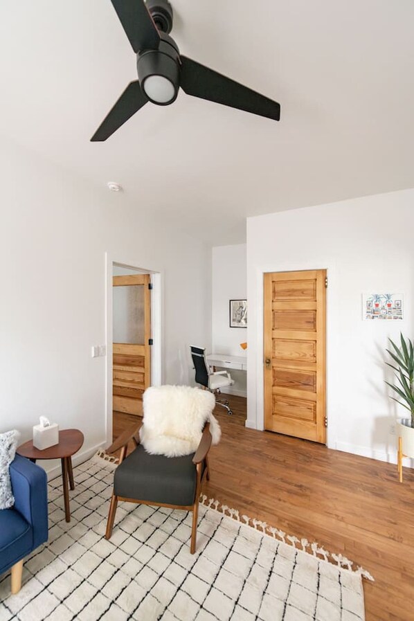 A modern living room with a ceiling fan, a blue sofa, a fluffy chair, and a wooden floor.