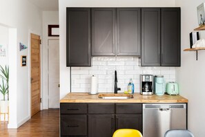 A compact kitchen with dark cabinets, a wooden countertop, a sink, a coffee maker, a toaster, and a dishwasher.