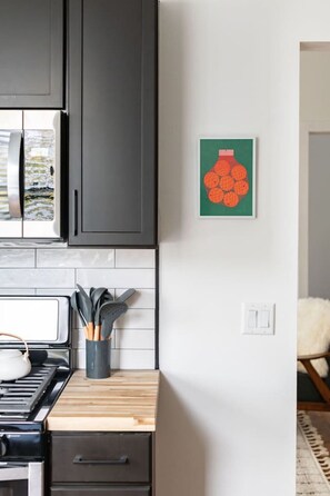 A kitchen with a microwave, stove, and a cutting board. There is a framed picture on the wall. - The Lincoln: Upscale 1 Bedroom Loft in downtown (Sioux Falls)