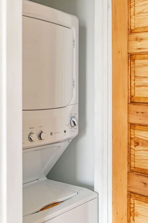 A white washing machine and dryer in a laundry room with a wooden door. - The Lincoln: Upscale 1 Bedroom Loft in downtown (Sioux Falls)