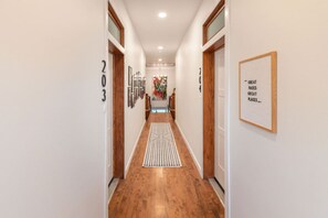 A hallway with wooden flooring, a central rug, and a framed inspirational quote on the wall.