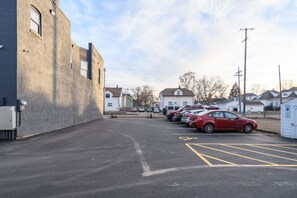 A parking lot with several cars parked in rows, a building with a flat facade on the left, and houses in the background. - The Lincoln: Upscale 1 Bedroom Loft in downtown (Sioux Falls)