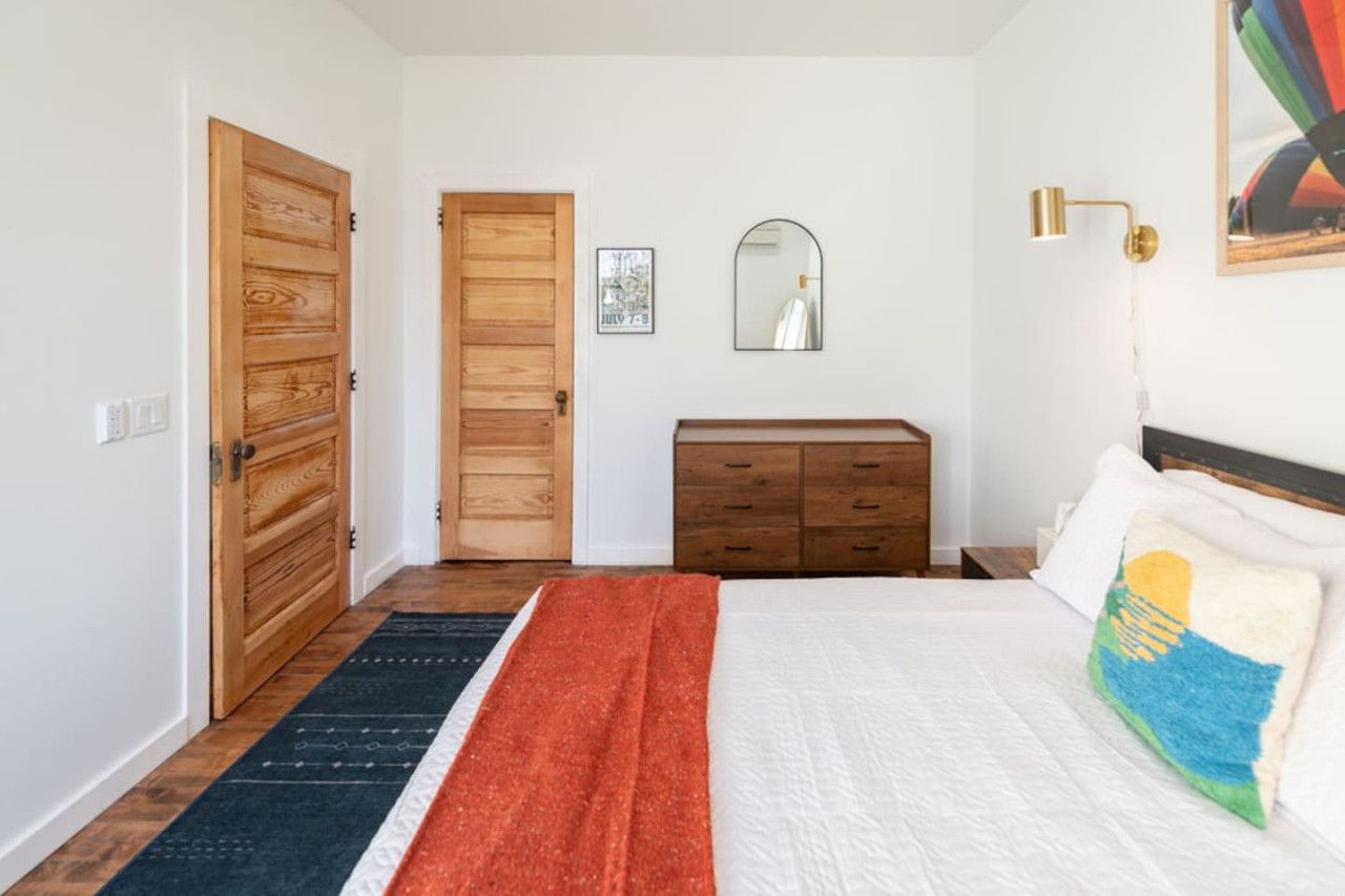 A bedroom with a bed, a dresser, a mirror, and a door.