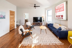 A living room with a sofa, chairs, a TV, and a ceiling fan. - The Roosevelt: Upscale Loft blocks from downtown (Sioux Falls)