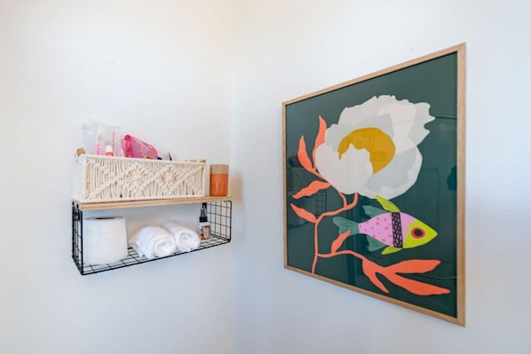 A wall-mounted shelf with toiletries and a framed artwork.