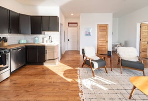 A modern kitchen with dark cabinets, a wooden countertop, and a dining area with a table and chairs.